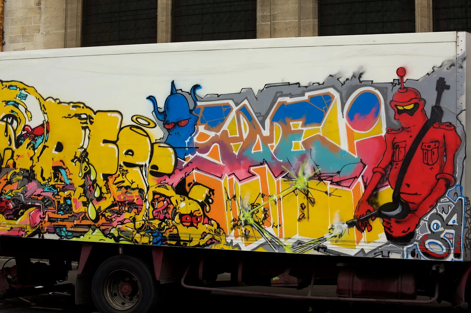 A parked truck covered from end to end in colorful graffiti lettering and painted characters on a city street.