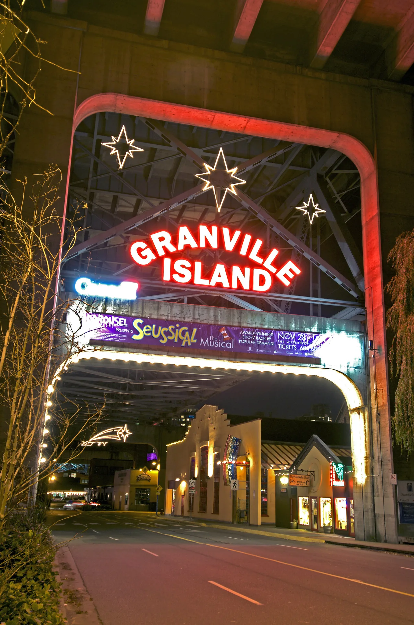 A neon sign reading Granville Island glows red over a road entrance at night, with lit buildings beyond.