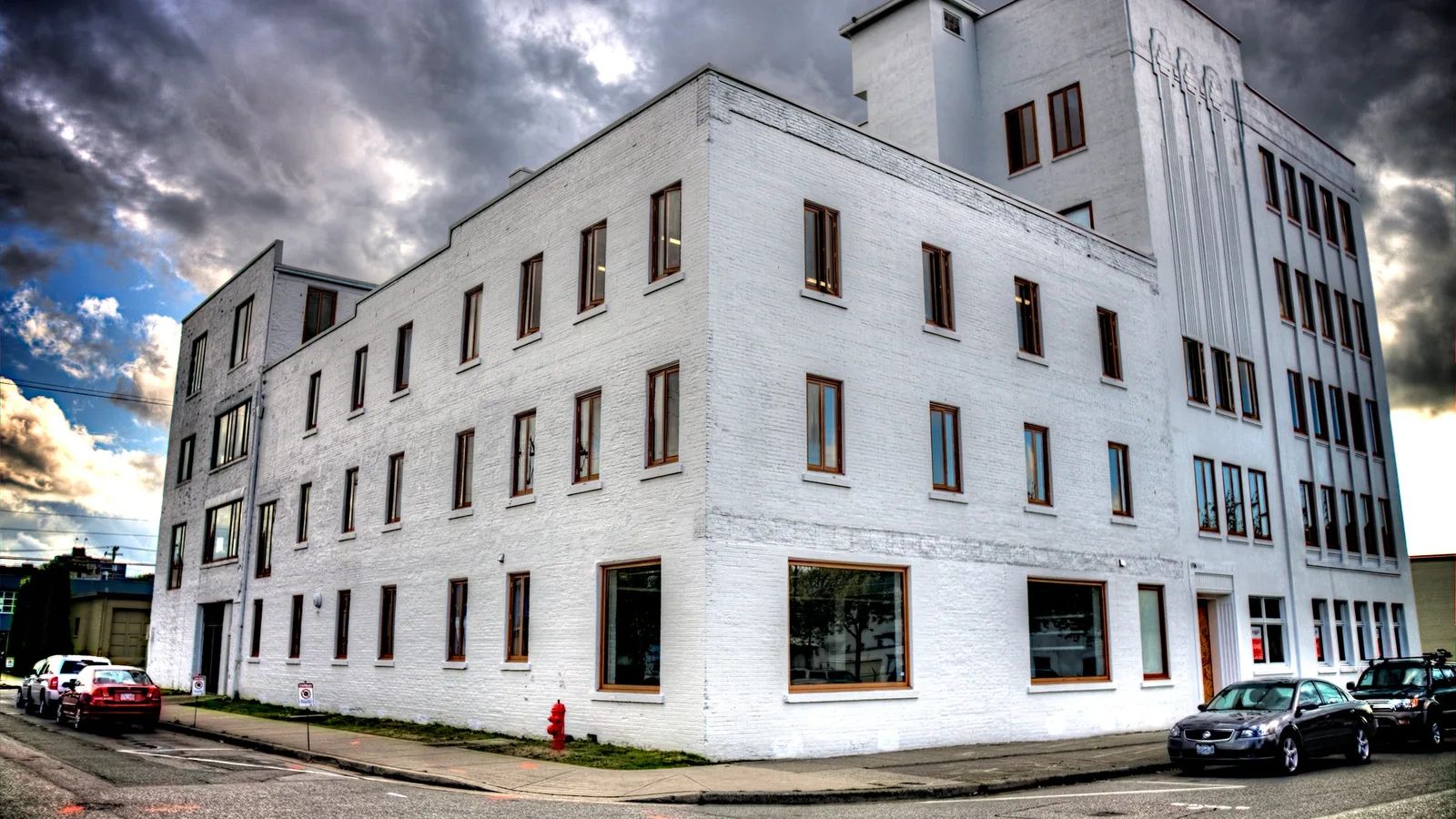 A bright white multi-storey building under a dramatic cloudy sky, its sunlit walls close to pure white