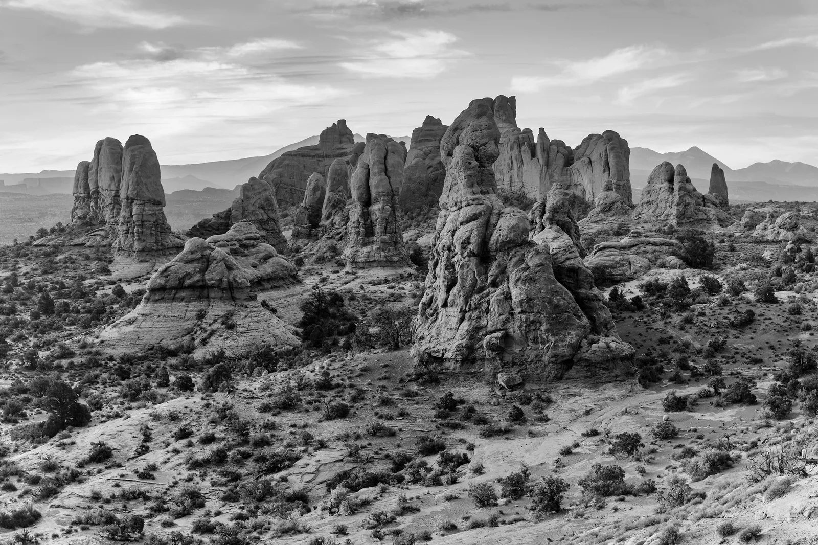 Black and white photo of rock fins and towers at Arches under soft, even light from a cloudy sky