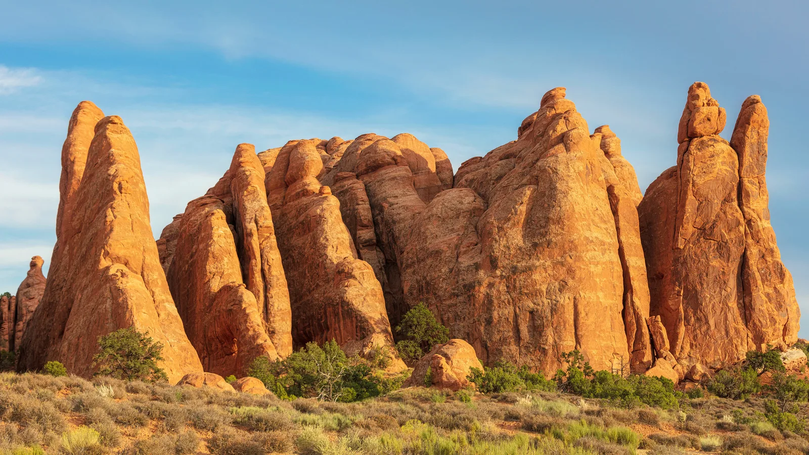 Red sandstone pillars glowing in warm sunlight against a clear blue sky, lit by a single strong light source
