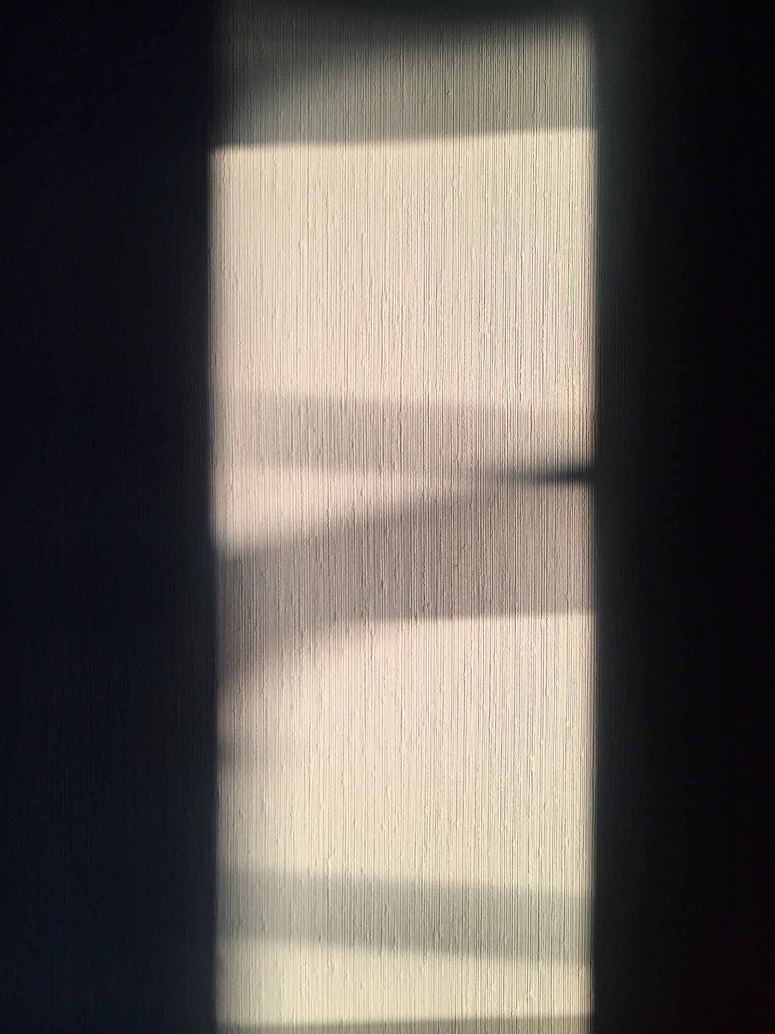 A narrow band of soft window light falling across a dark patterned wall, with deep shadow on either side
