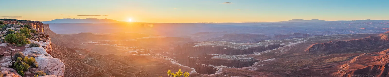 Wide sunrise view over layered canyon country with the sun on the horizon