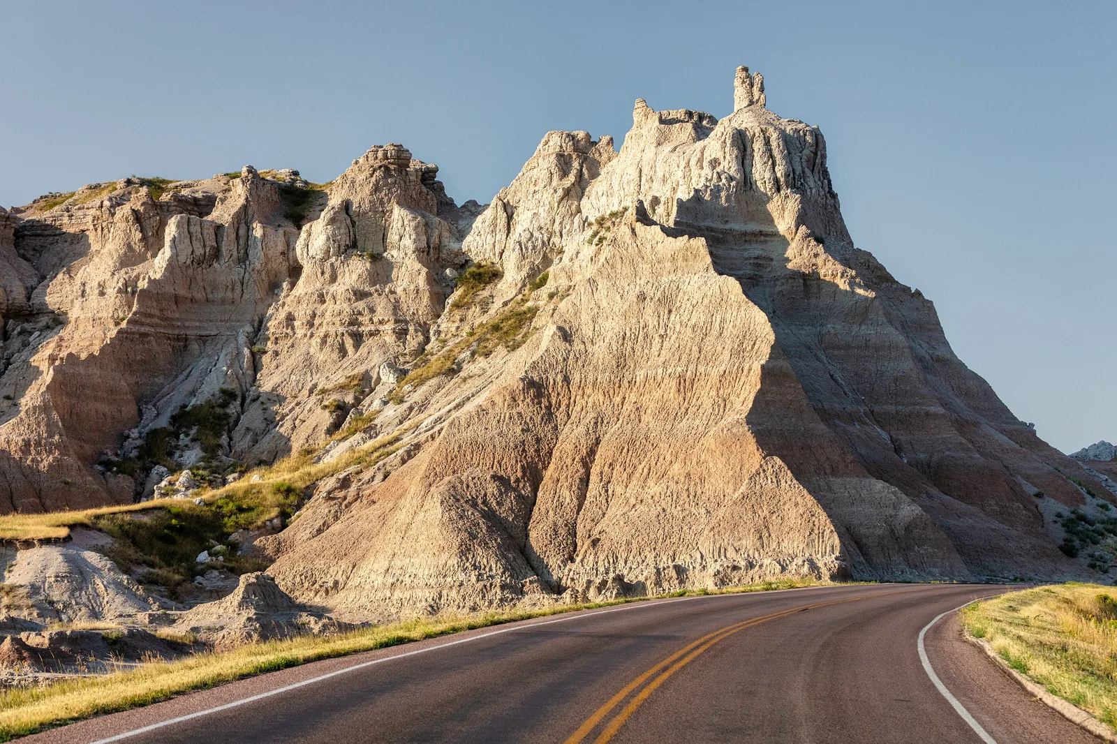 A road curving past jagged badlands formations, with deep shadows on one side of the rock giving it strong shape
