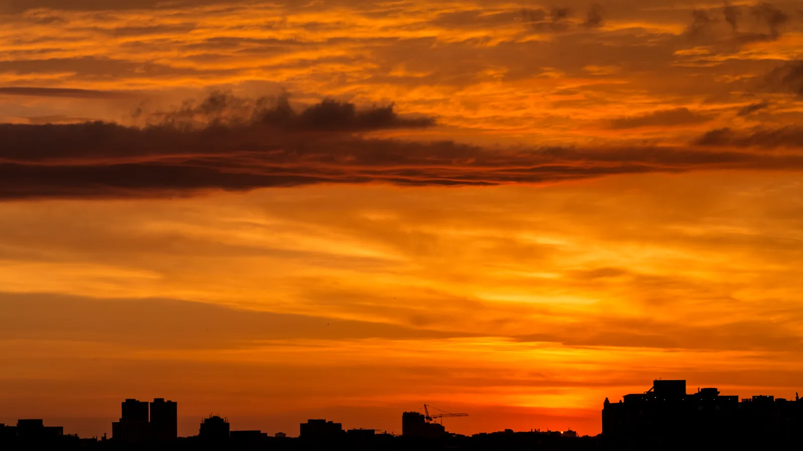 Broken cloud glows deep orange across the sky above the dark silhouette of a city skyline.