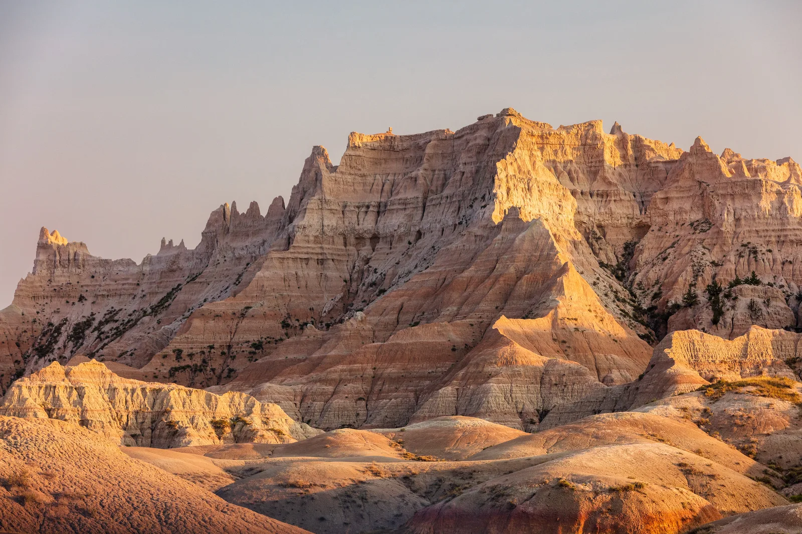 Eroded badlands formations glowing warm orange at sunset against a pale sky