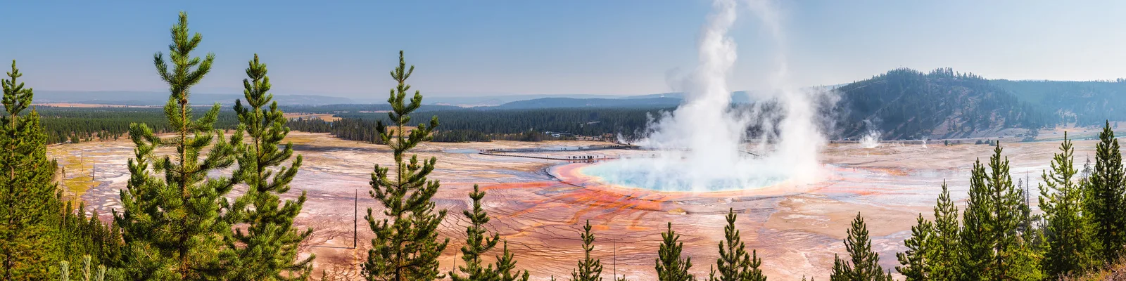 Steam rising from a colorful hot spring basin under a blue sky with scattered clouds