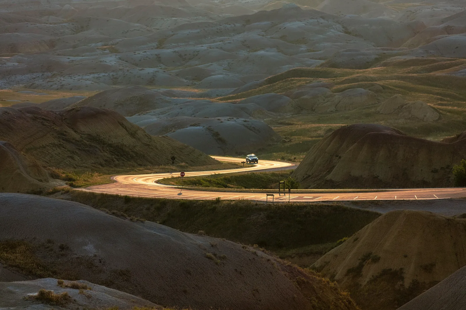 A winding road glowing gold in low evening light with soft blurred hills behind