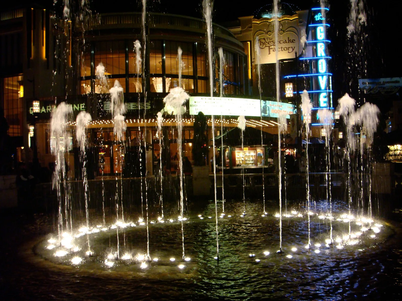 A lit fountain at night, with bright points of light reflecting off the falling jets and the wet pavement