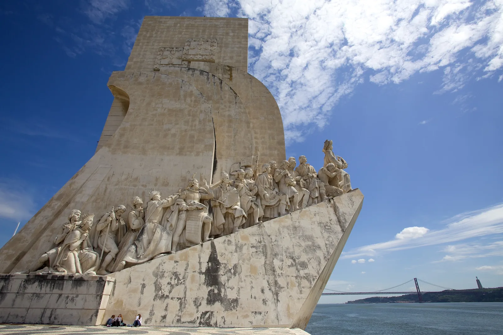 A towering stone monument shaped like a ship's prow, lined with carved figures, against a deep blue sky with white clouds.