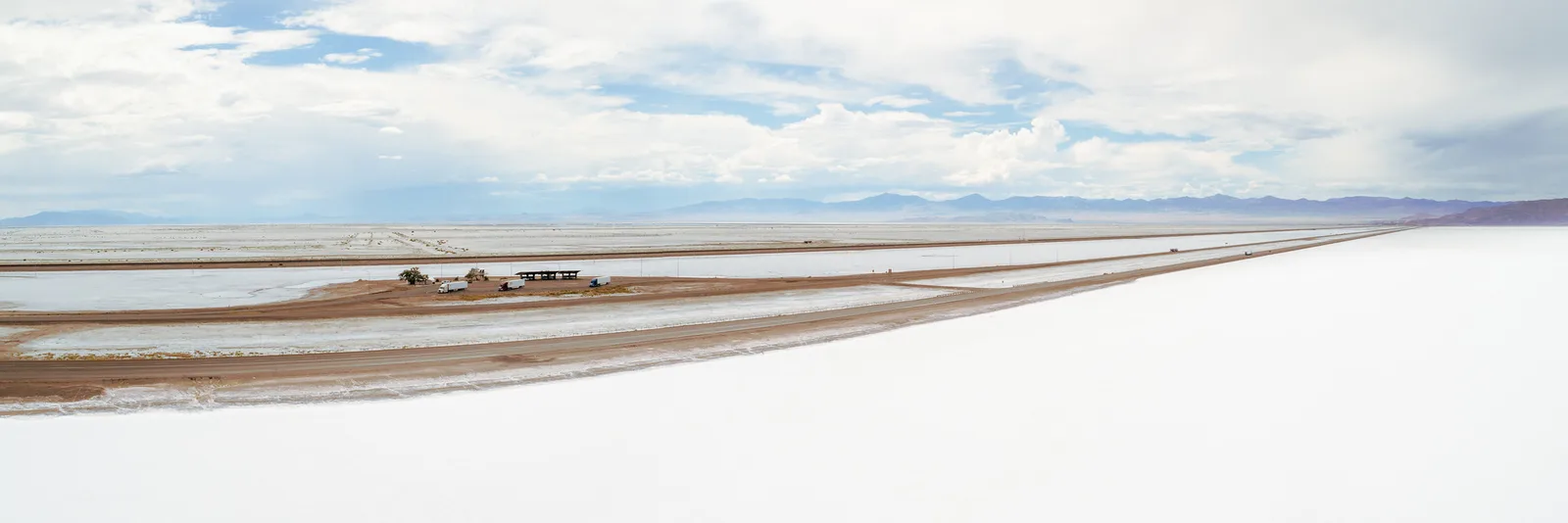 A straight highway runs to the horizon across flat white salt flats under a wide sky with scattered clouds.