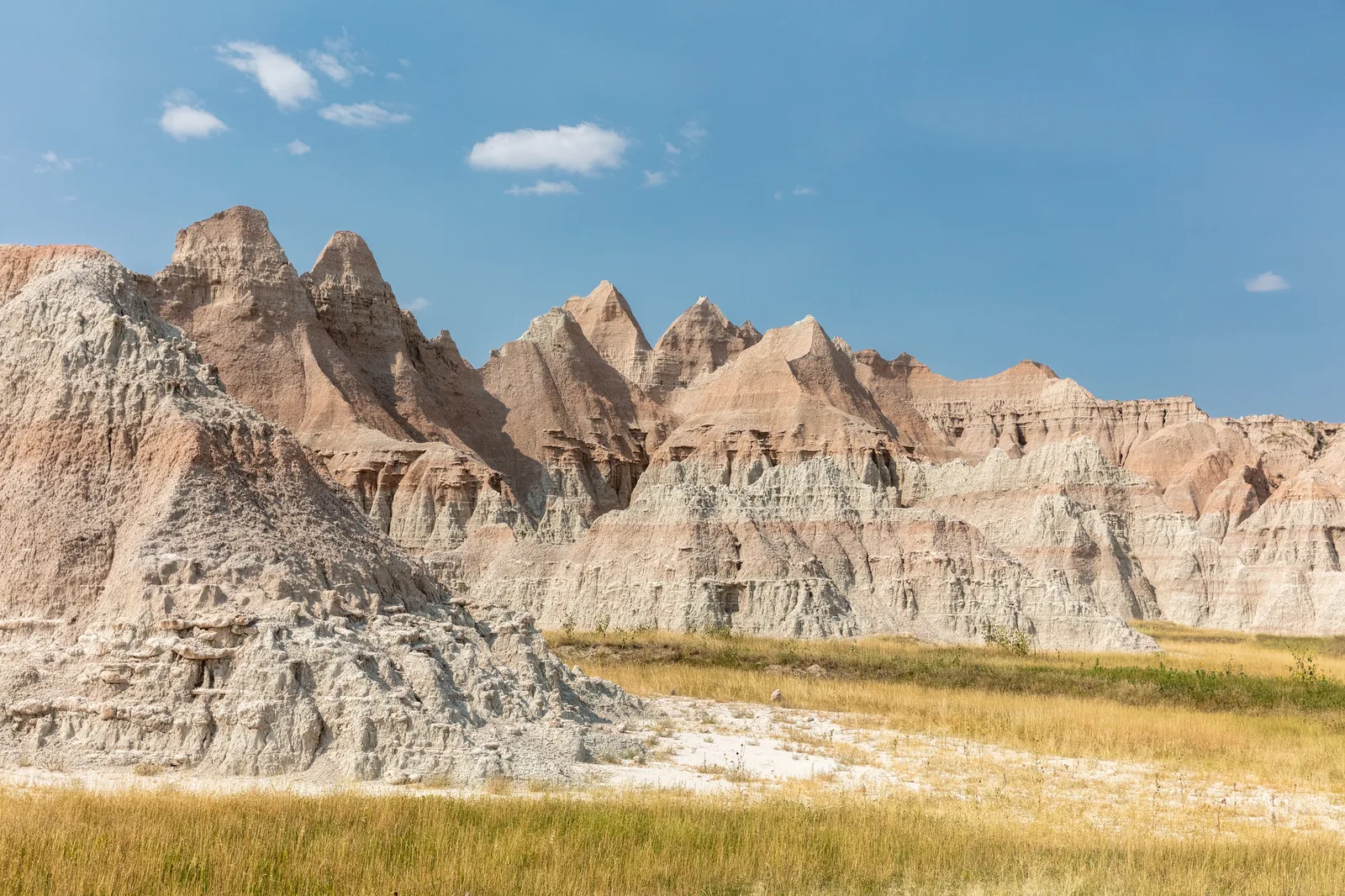 Jagged gray and tan badlands peaks rising above golden grass under a blue sky