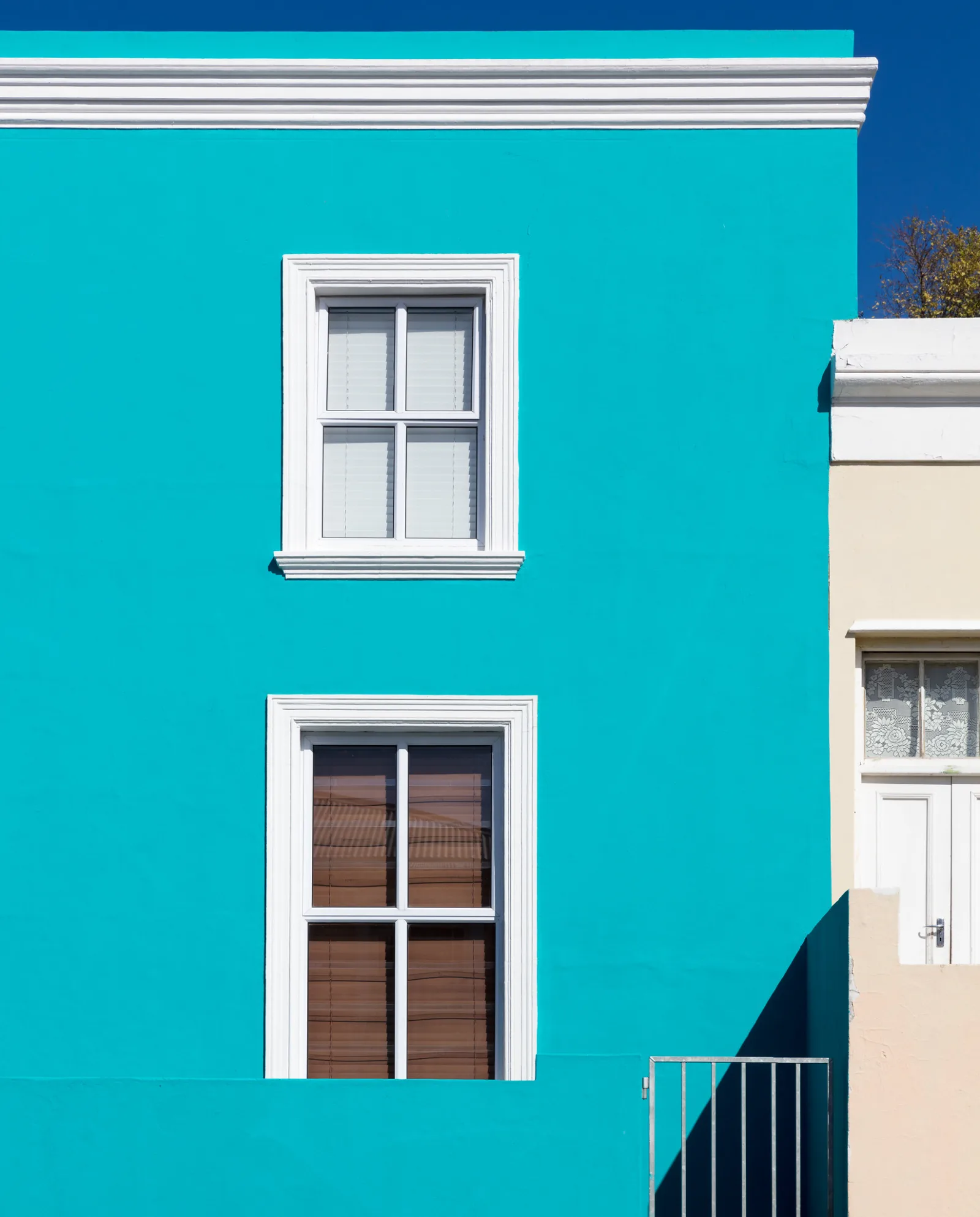A bright teal building wall has two white-framed windows, one above the other.