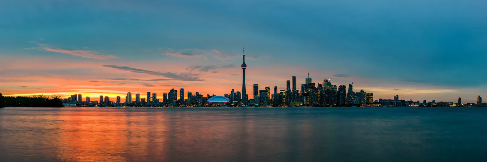 A very wide view across calm water to a distant city skyline with a tall tower, with nothing close to the camera.