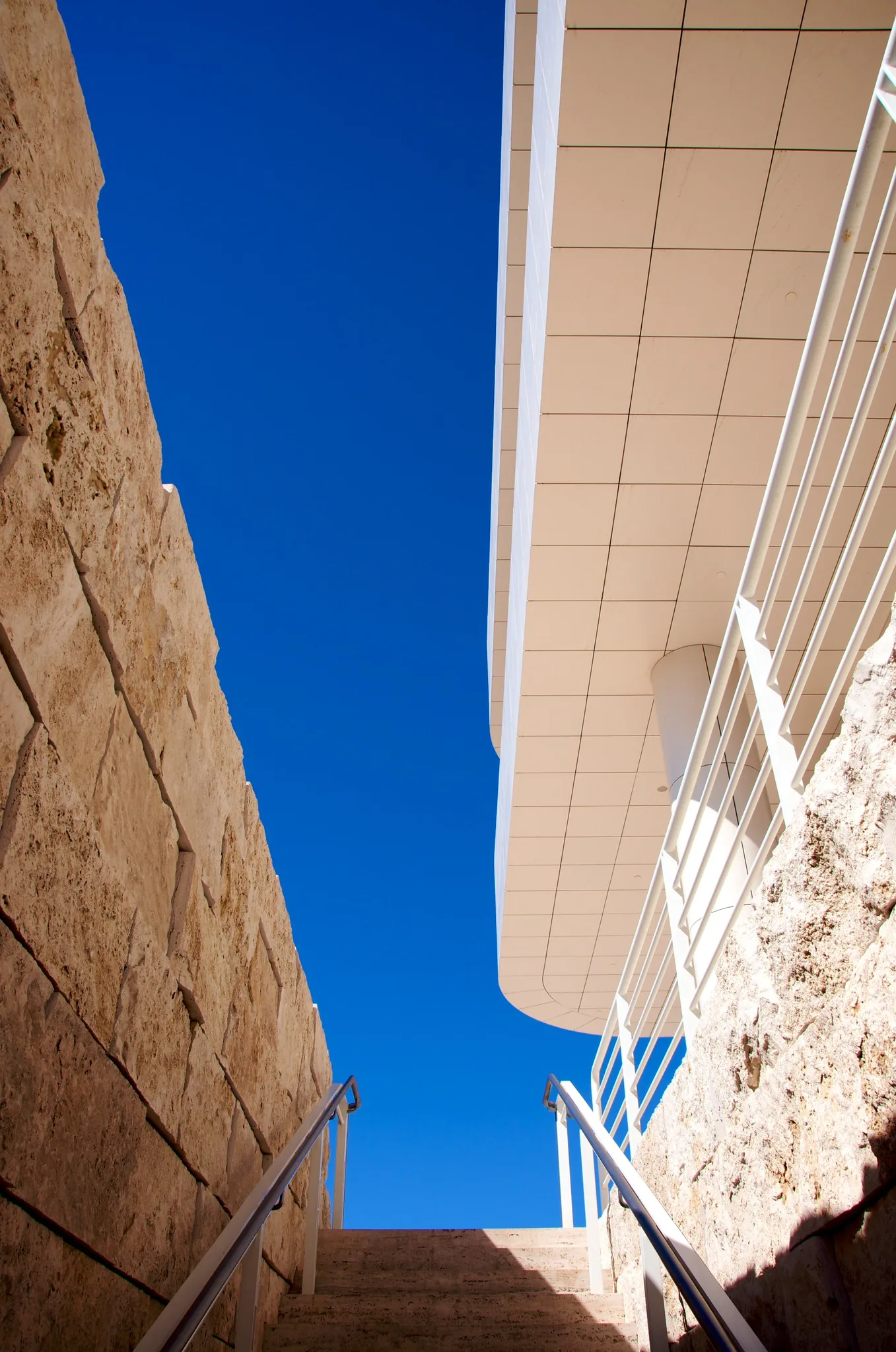 Looking up a stone staircase between pale walls toward a deep blue sky