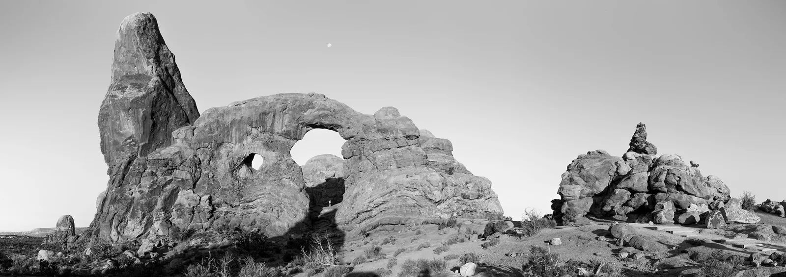 Black and white photo of Turret Arch standing out as a dark shape against a pale, almost white sky